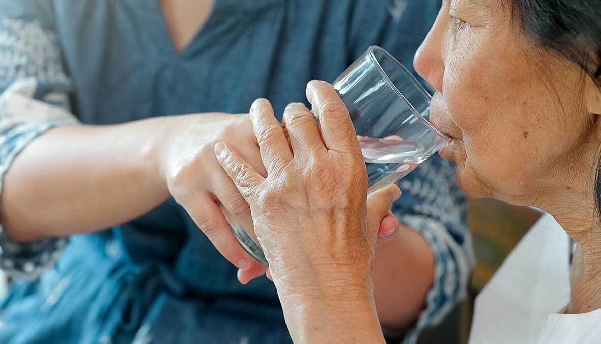 Caregiver gives elderly woman glass of water for hydration